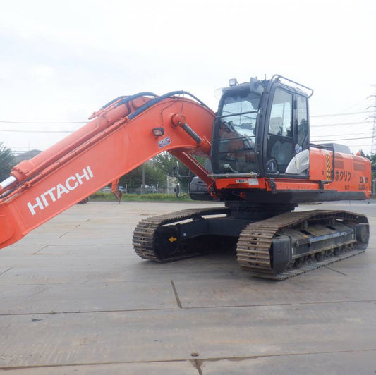 Orange Hitachi excavator on a concrete surface with trees and power lines in the background.
