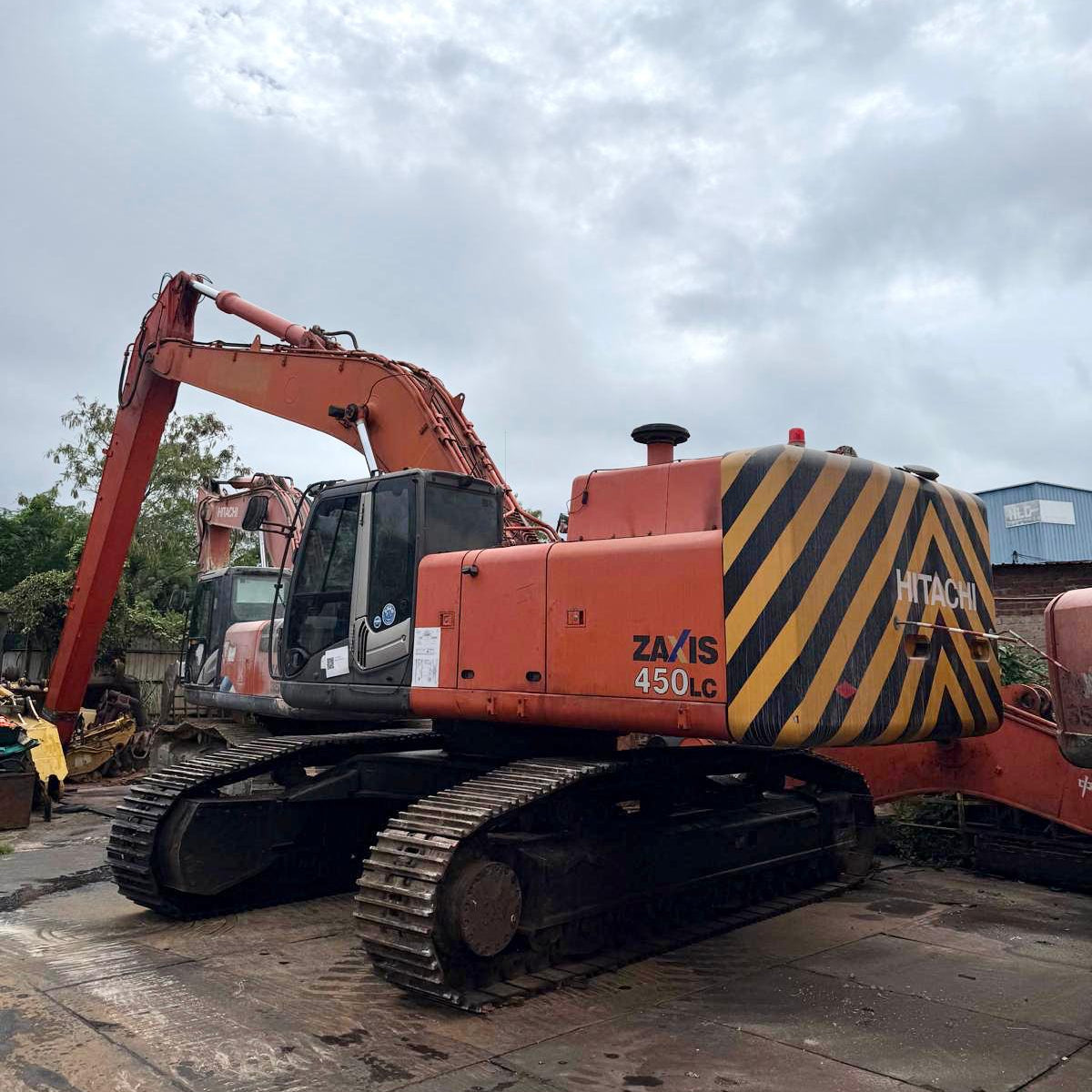 Orange Hitachi excavator with black and yellow striped pattern on a cloudy day.