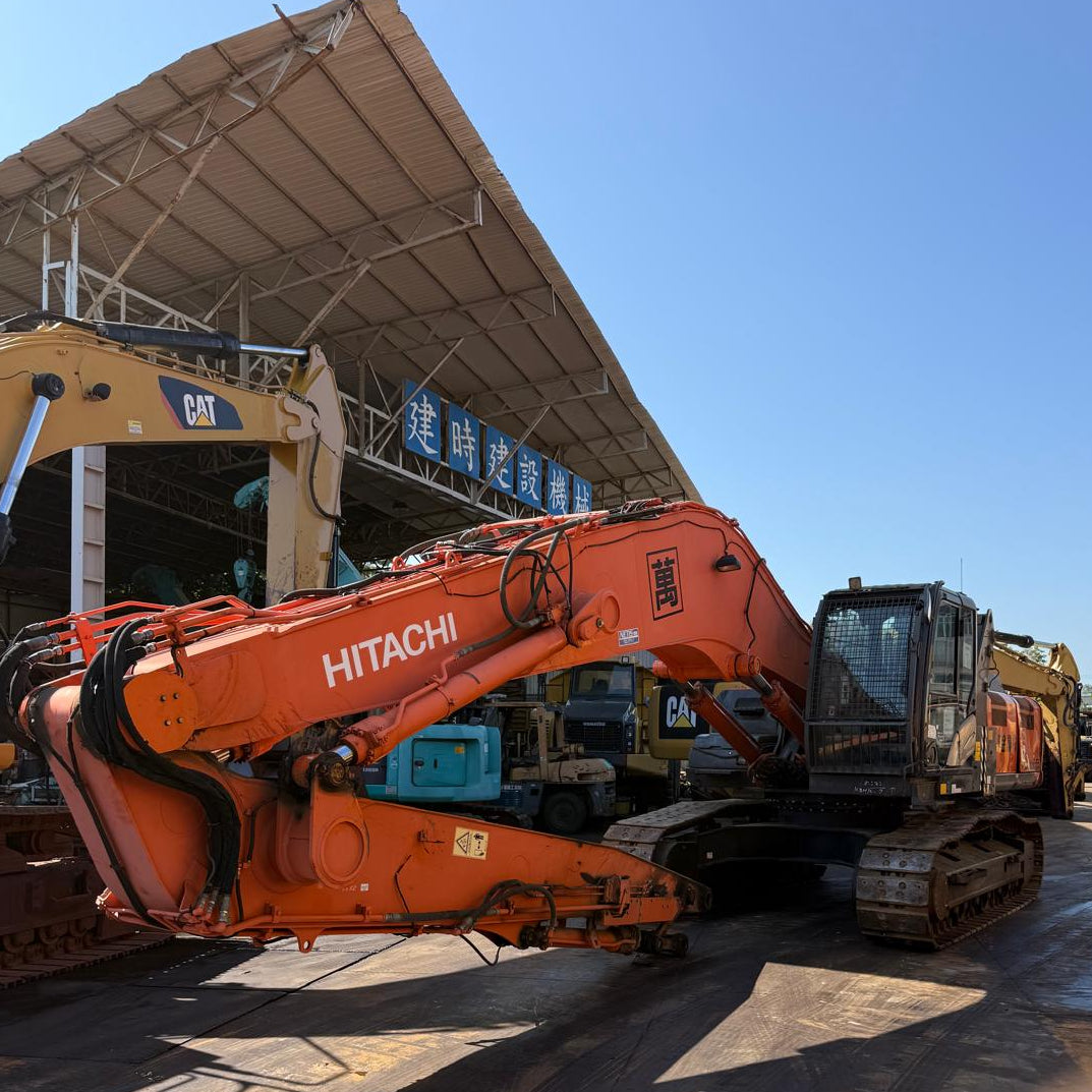 Orange Hitachi excavator in a warehouse setting with blue sky.