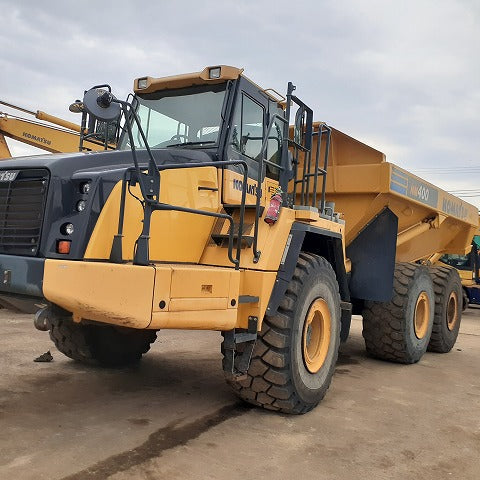 Large yellow construction vehicle on a dirt field with other equipment in the background.