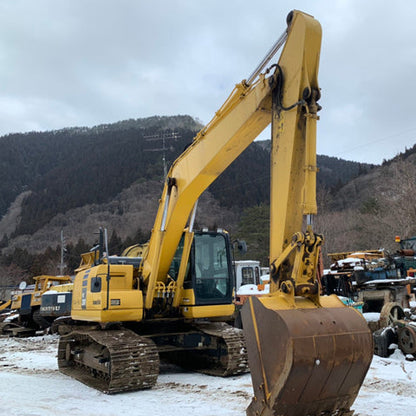 Yellow excavator in a snowy outdoor setting with mountains in the background