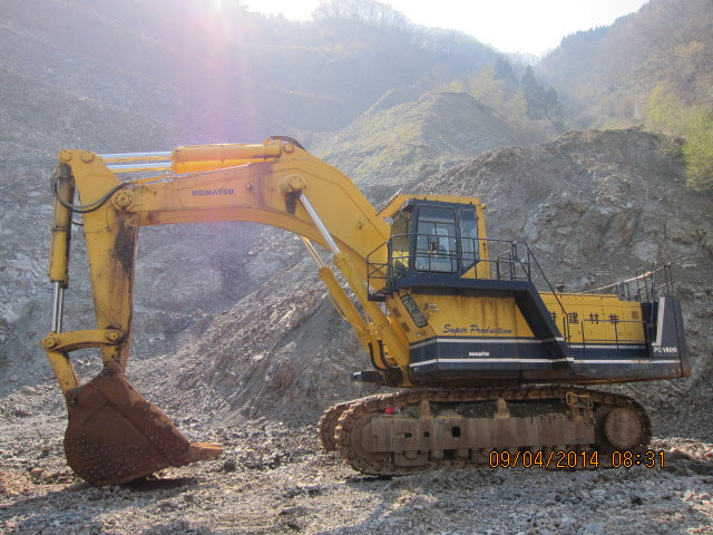 Yellow excavator on a rocky terrain with mountains in the background