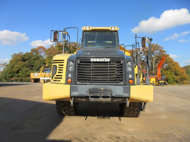 Komatsu dump truck on a dirt road with trees and blue sky in the background