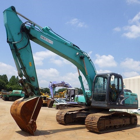 Large green kobelco excavator on a construction site with a clear blue sky.